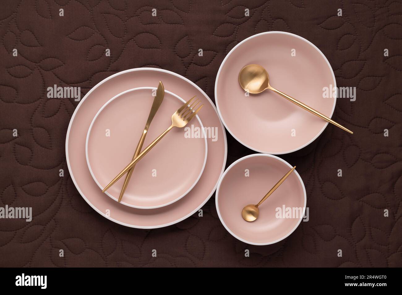 A set of round beige plates of different sizes on the table, top view. Golden cutlery and serving utensils. An empty dishes on a dark brown fabric tab Stock Photo