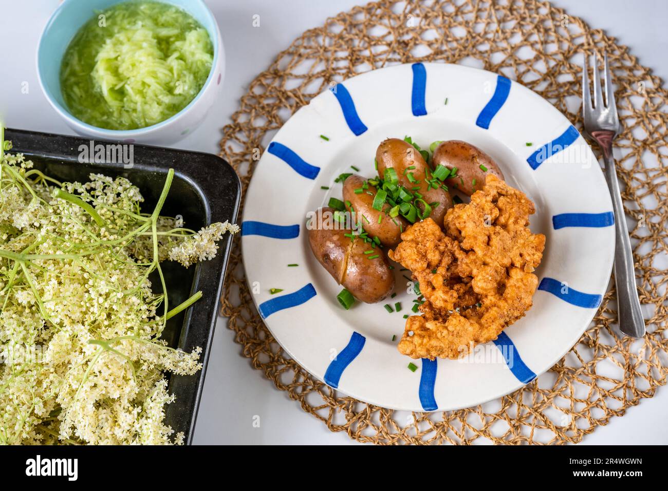 Plate with fried elder flower in dough and potato, elder flowers on baking pan and cucumber salad on table. Stock Photo