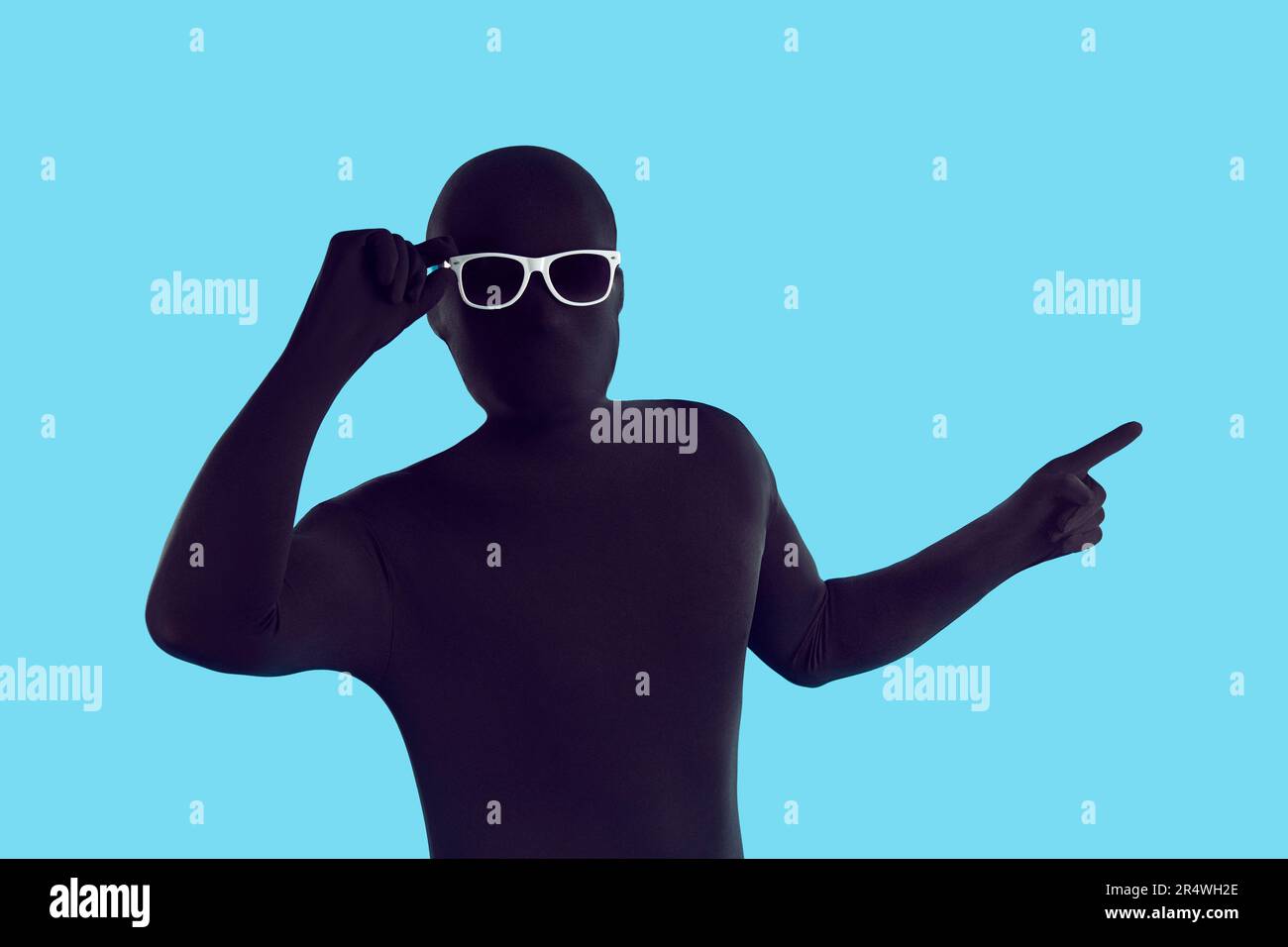 Funny man disguised in black bodysuit and sunglasses pointing away to show something Stock Photo