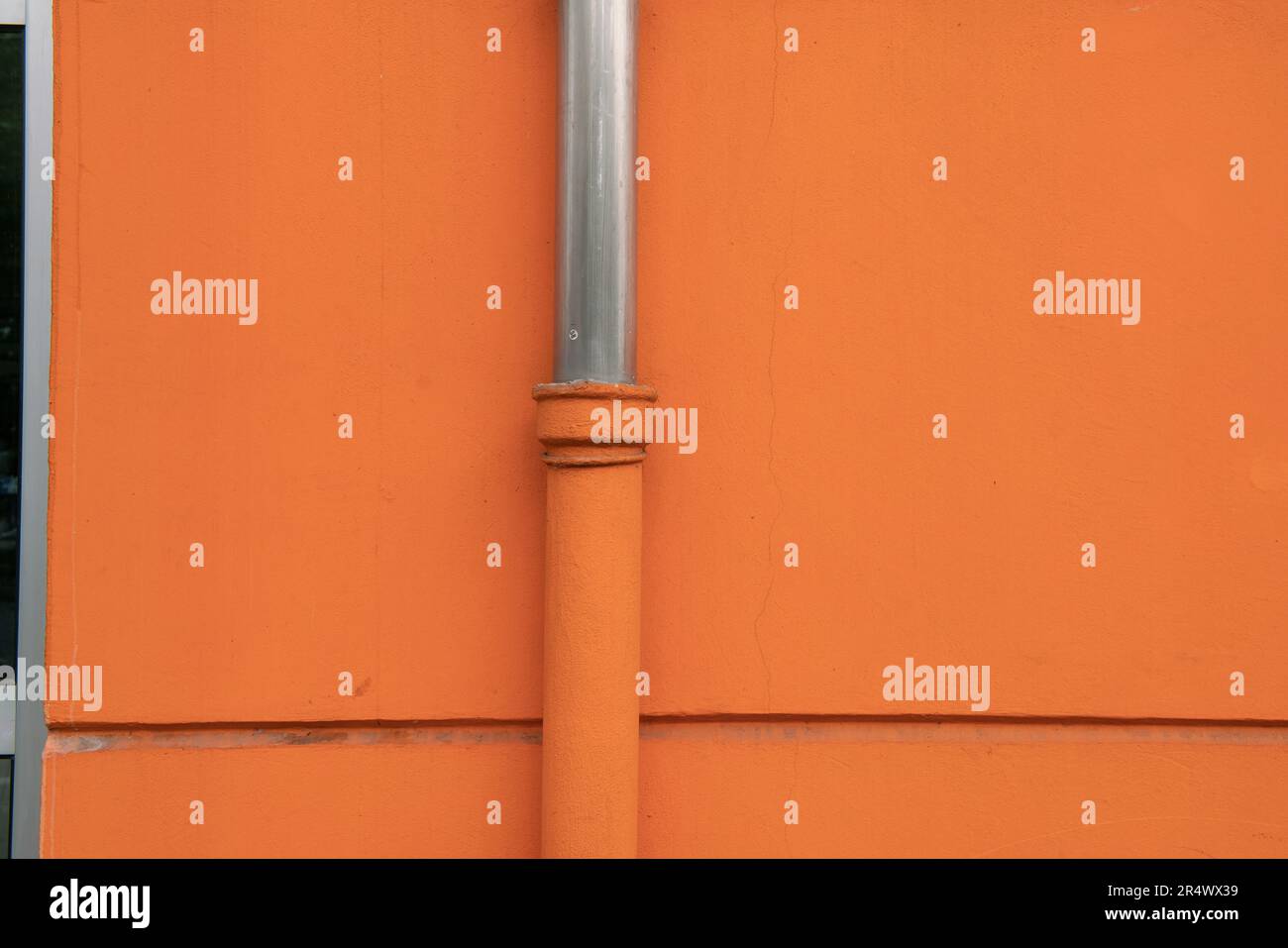eaves or downspout, particular house of the facade on a building with orange plaster. stainless steel water drain pipes Stock Photo
