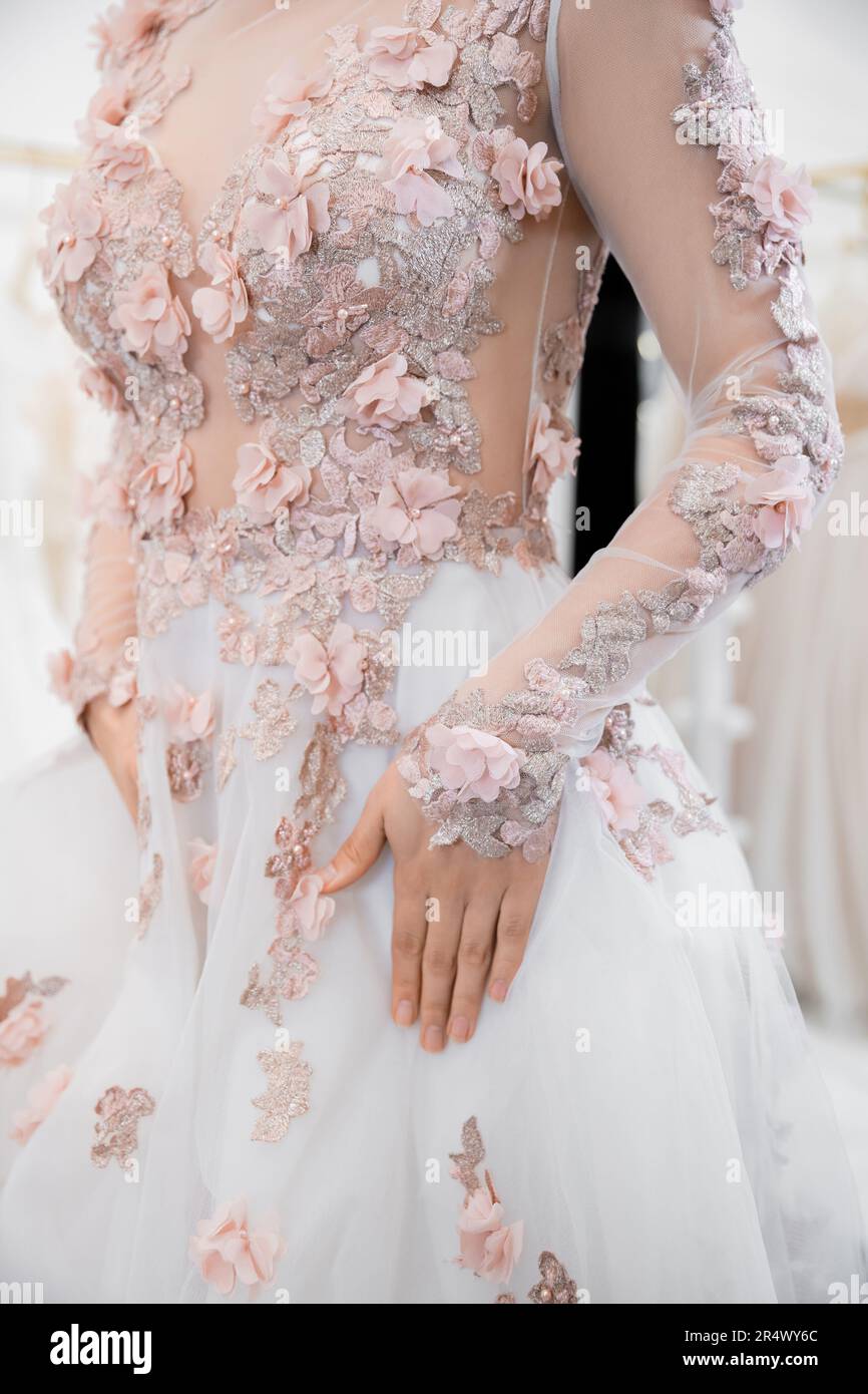 cropped view of woman standing in gorgeous and floral wedding dress inside of luxurious salon around blurred white tulle fabrics, bridal shopping, bri Stock Photo