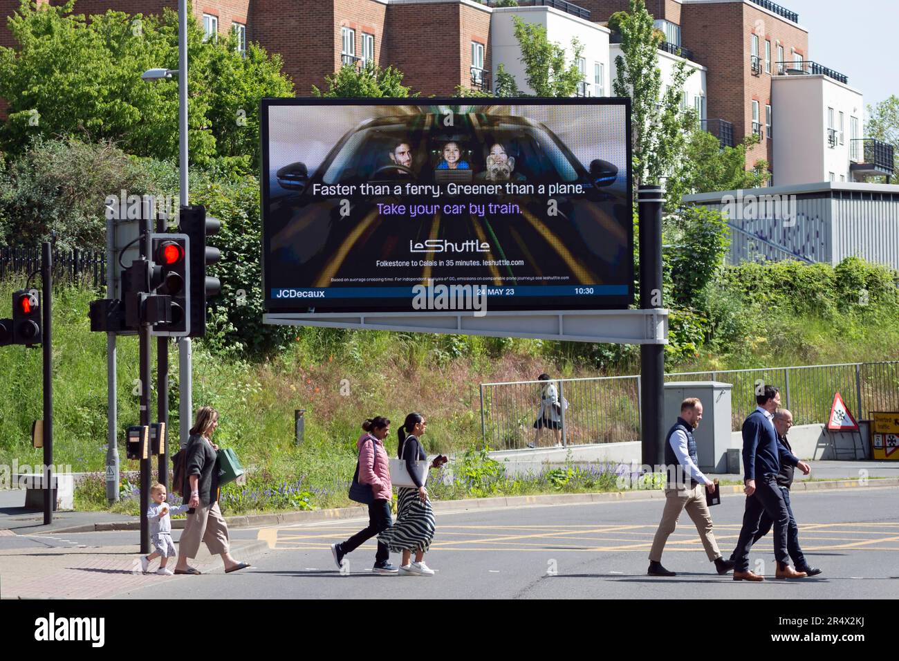 pedestrians cross the road in kingston, surrey, england, in front of a digital billboard advertising le shuttle, a train link from the uk to europe Stock Photo
