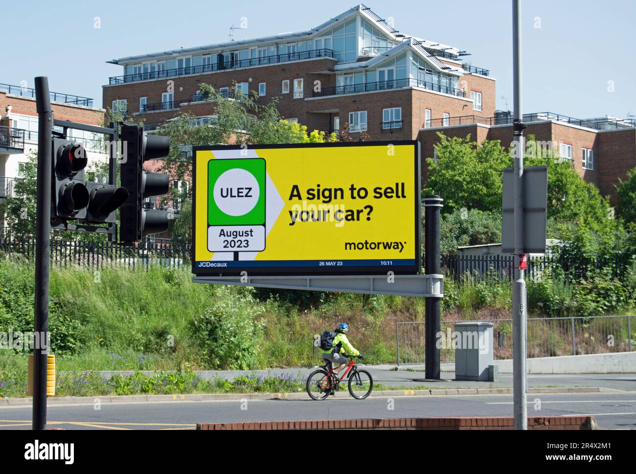 a cyclist passes a digital billboard displaying an advert from the car market company motorway, noting the august 2023 start of the new ulez scheme Stock Photo