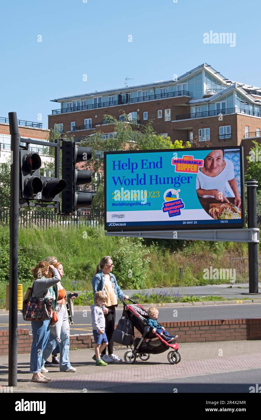 pedestrians wait at a crossing in kingston, surrey, england, in front of a digital billboard advertising world hunger day, 28 may 2023 Stock Photo