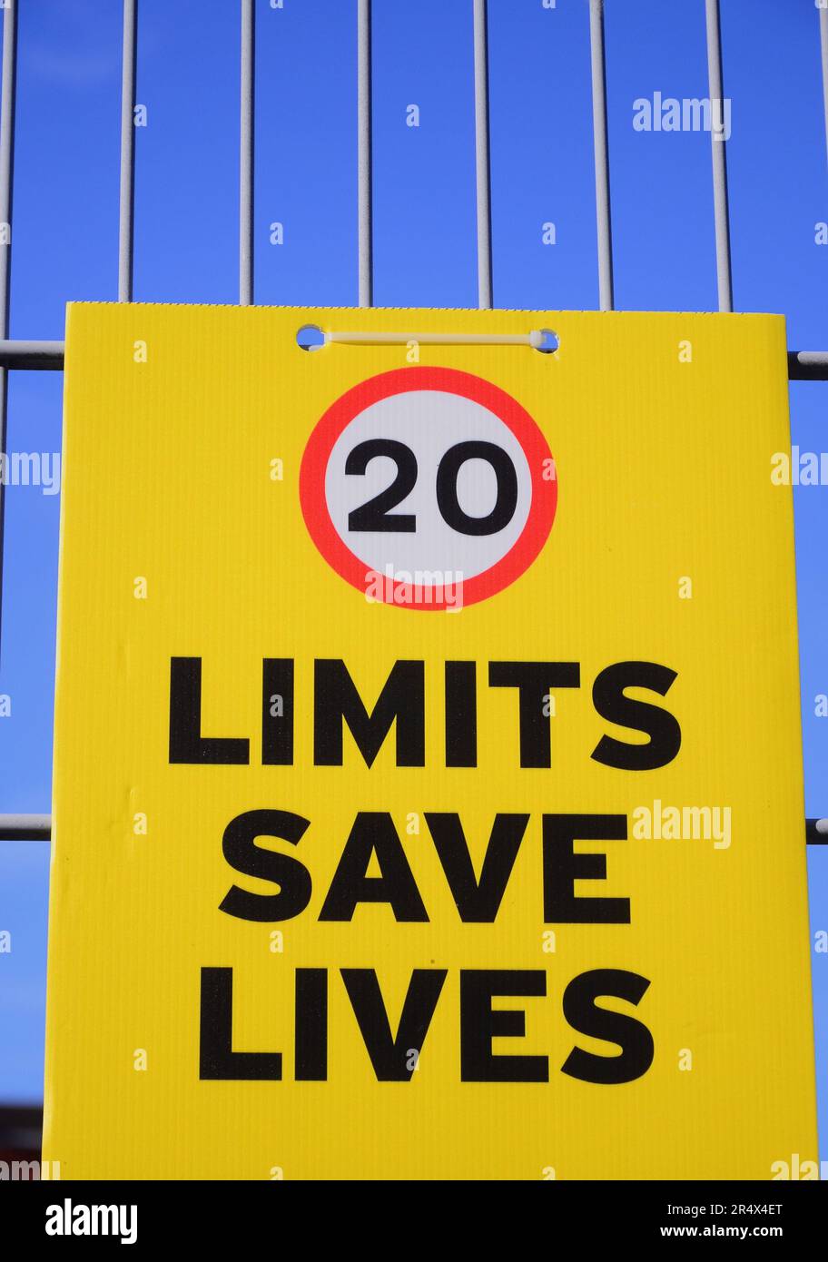 Speed limit placard says 'Limits Save lives' with 20 miles per hour image on the fence of a school in Manchester, UK Stock Photo
