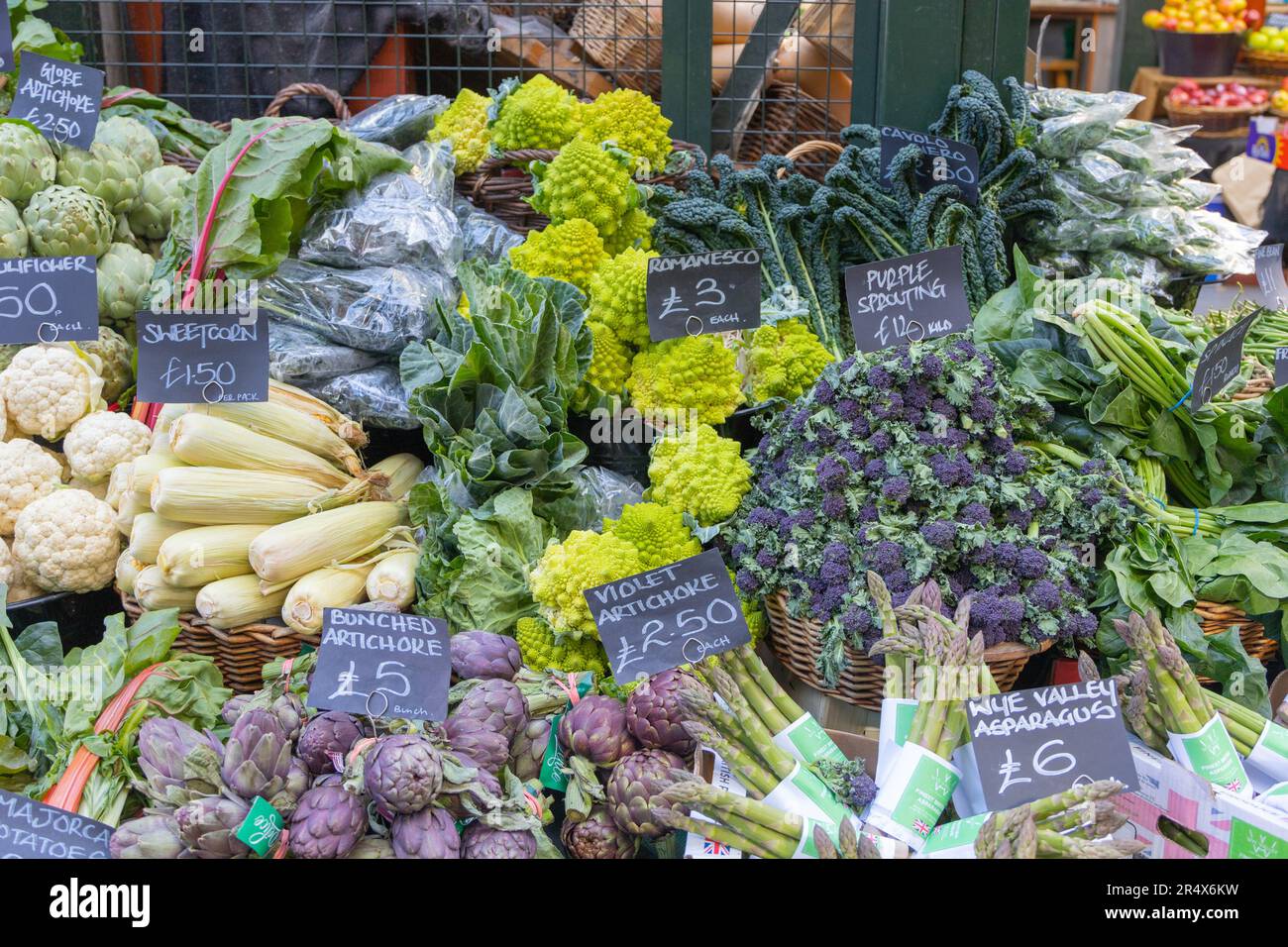 Fresh vegetables on a stand at a food market in the UK including, Romanesco, artichoke, corn, cauliflower, and asparagus. No people. Stock Photo