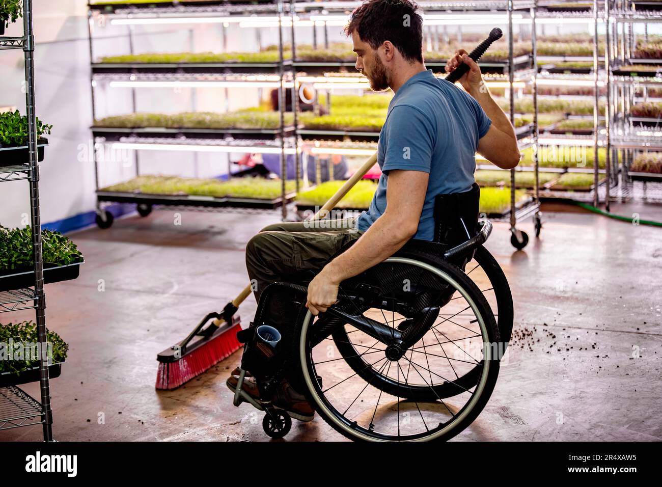 Male worker in a wheelchair sweeps the floor between shelves of