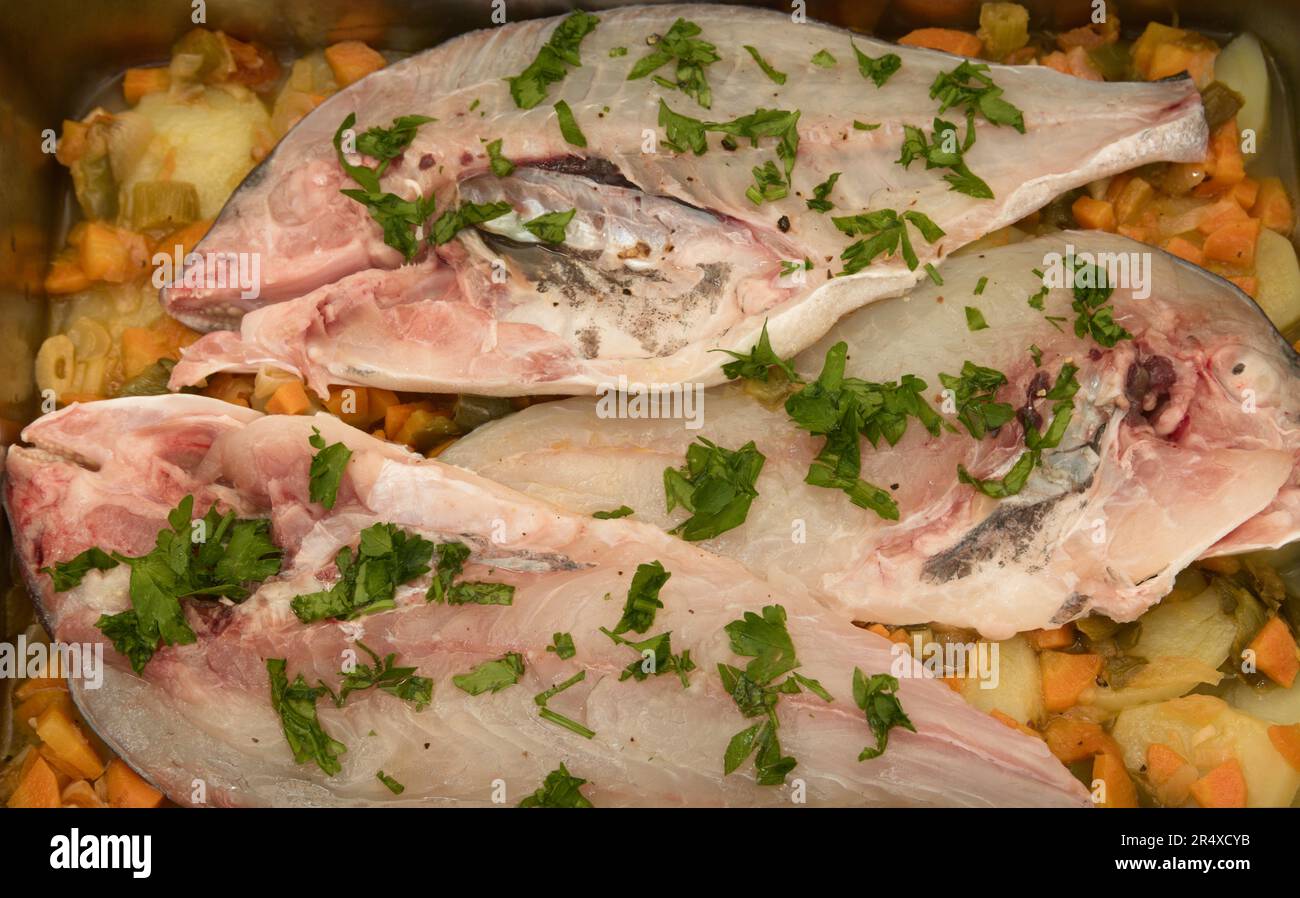Flat lay of the preparation of a recipe for three halves of baked sea bream with vegetables and parsley Stock Photo
