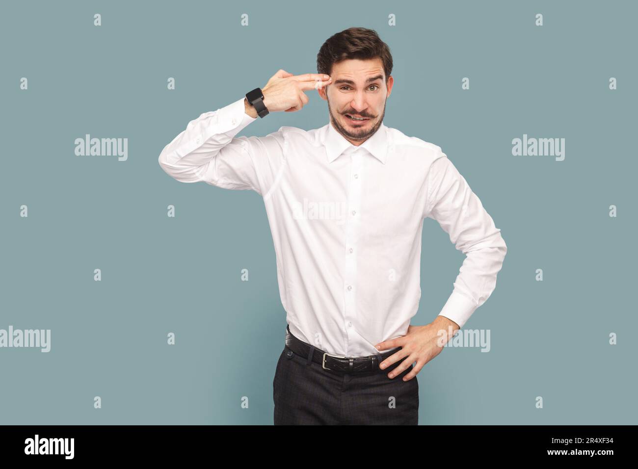 Portrait of depressed attractive man with mustache holding fingers gun near his temple, being in bad mood and stress, wearing Indoor studio shot isolated on light blue background. Stock Photo