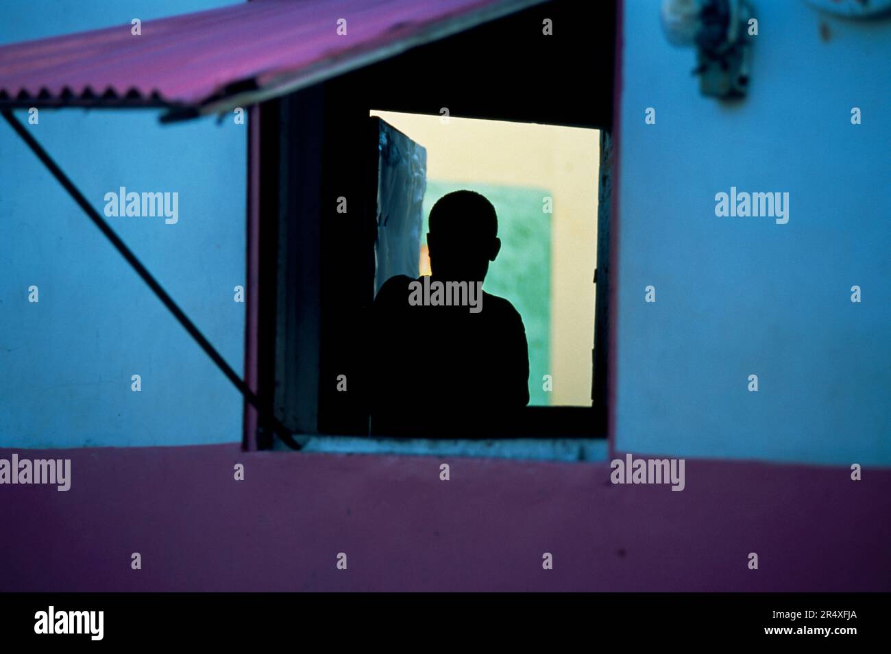 Silhouette of a boy looking through an open window of a colorful building; Commonwealth of Dominica Stock Photo