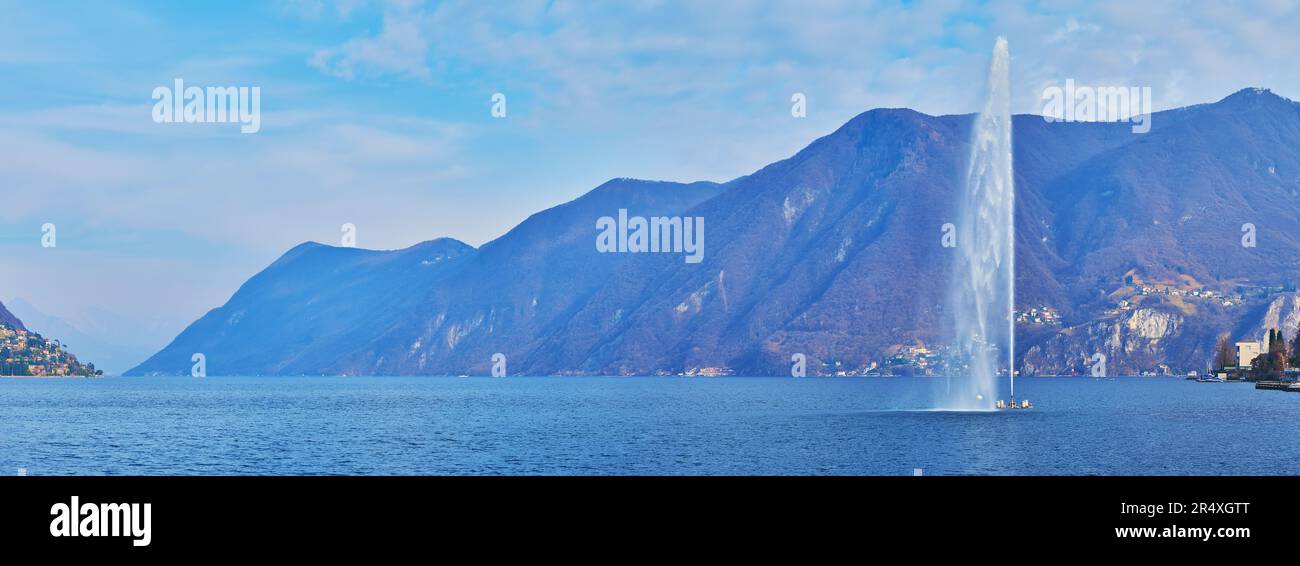 Panorama of crystal clear Lake Lugano with Getto d'Acqua (Water Jet on the bay of Lugano) fountain, hazy Alps and Monte Sighignola, Lugano, Ticino, Sw Stock Photo