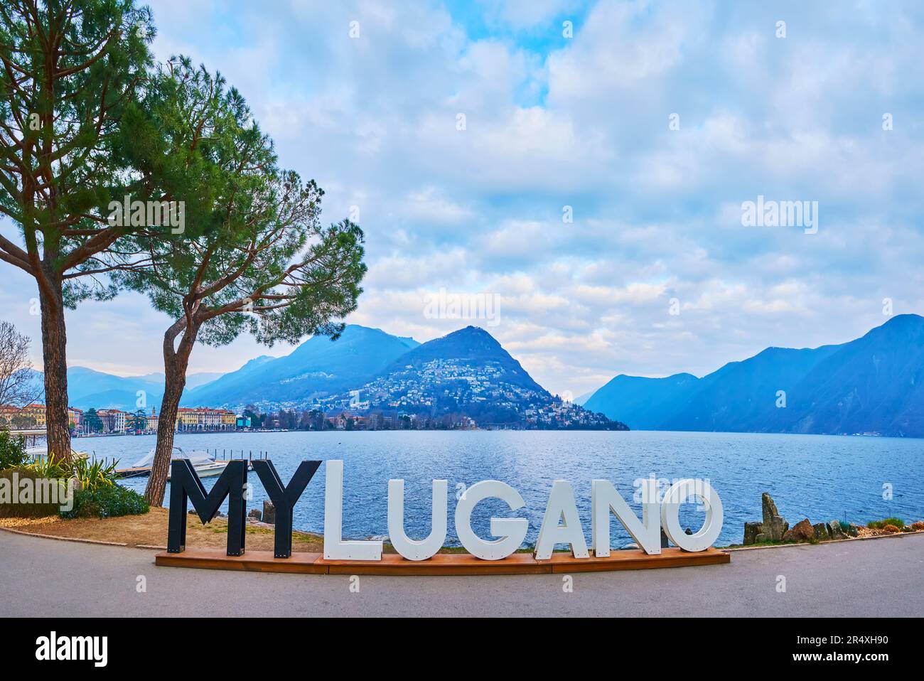 LUGANO, SWITZERLAND - MARCH 14, 2022: The black and white MyLugano sign on pedestrian embankment of Lake Lugano against Monte Bre at dusk, on March 14 Stock Photo