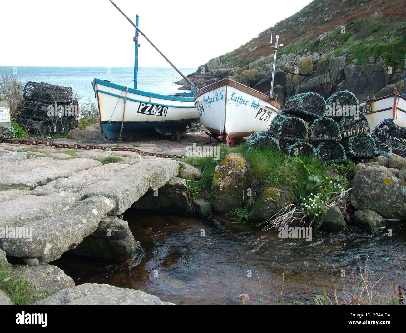 Crab and lobster pots and fishing boats with the old bridge over the stream in Penberth Cove Harbour, Cornwall, England, UK. Stock Photo