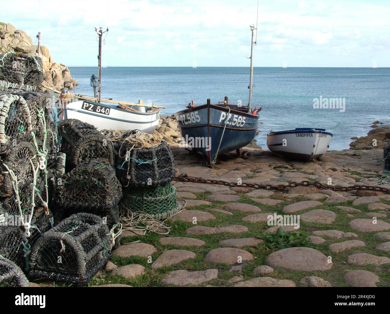 Crab and lobster pots and fishing boats above the slipway at Penberth Cove Harbour, Cornwall, England, UK. Stock Photo