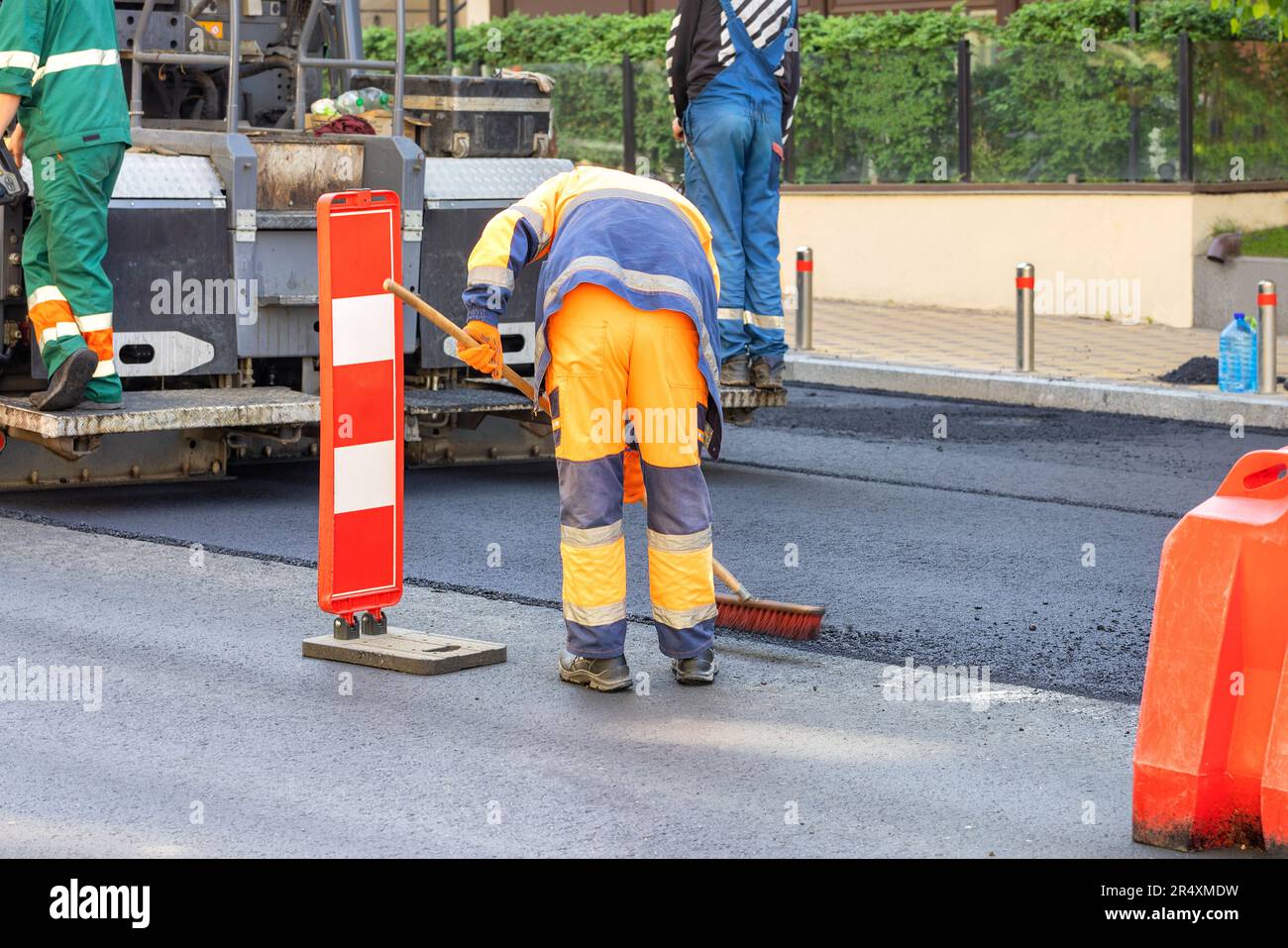 Road builders make asphalt repairs on an asphalt paver and sweep excess gravel with a nylon brush. Stock Photo