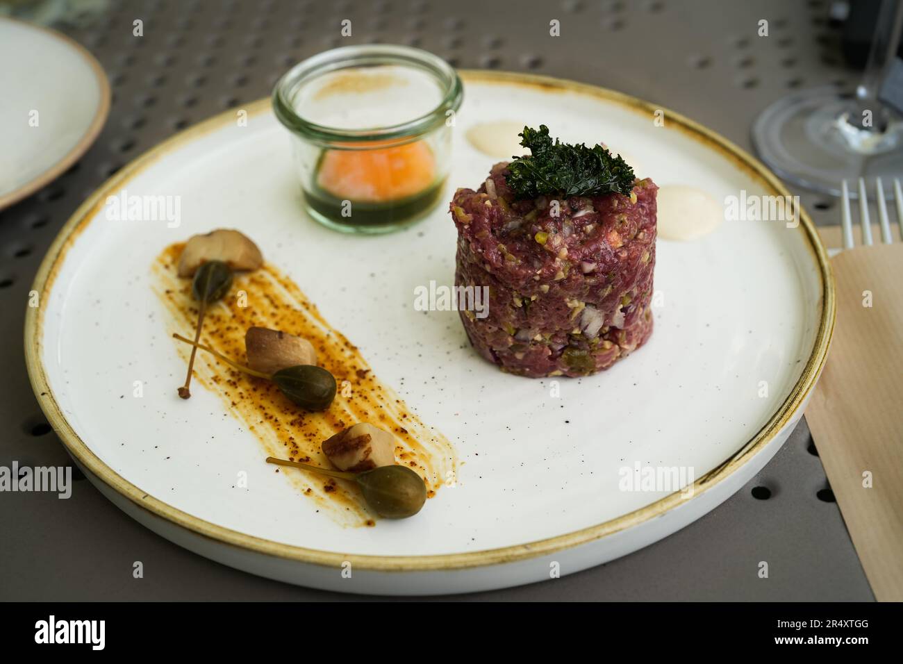 Steak tartare with raw ground beef, kale, raw egg yolk, and capers on a white plate with a golden rim. Keto diet, raw healthy eating gourmet Stock Photo