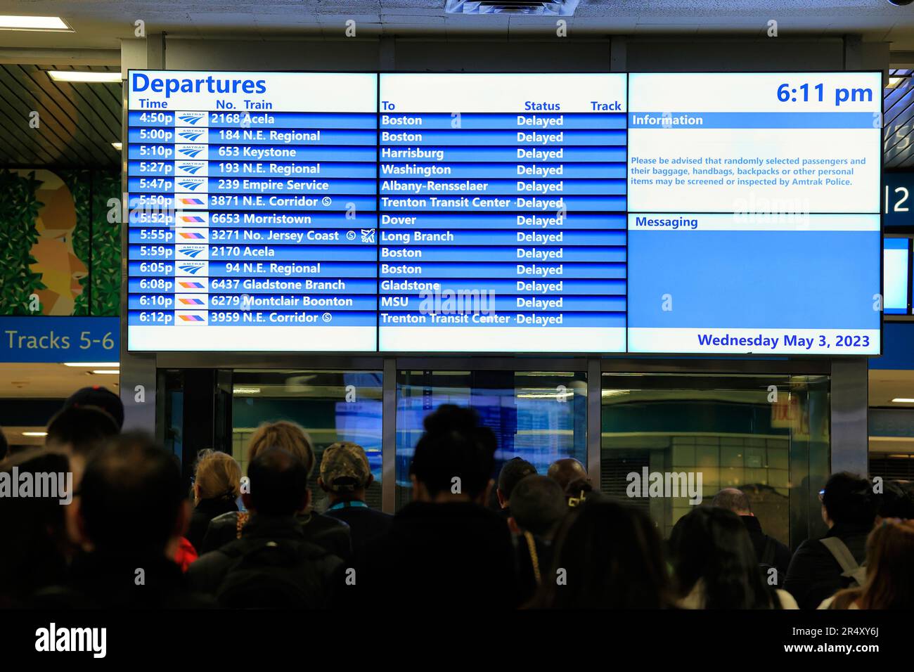 Rush hour commuters wait by a train departure board at Penn Station, New York, as trains are delayed for hours due to police activity, May 3, 2023. Stock Photo