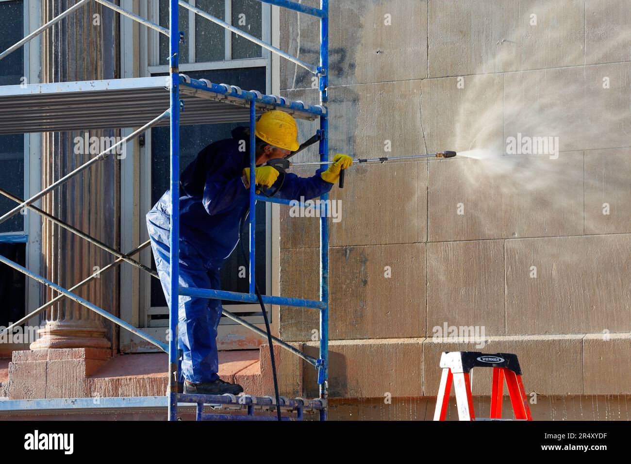 A worker power washing graffiti and dirt off a New York City school building with a high pressure spray gun. Stock Photo
