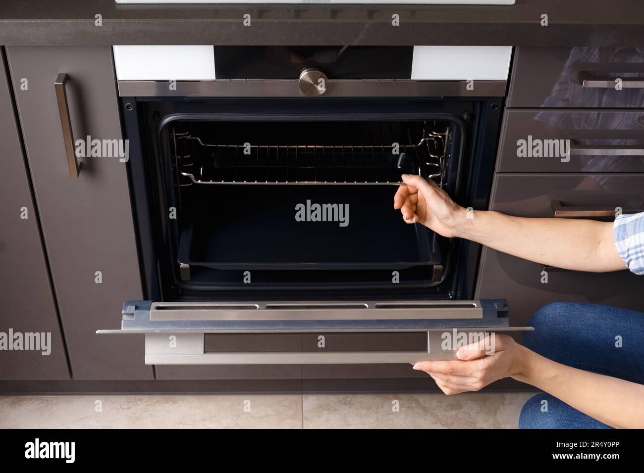 The girl opens the built-in oven door and takes out a baking sheet. Built-in oven with display in a modern kitchen interior. Stock Photo