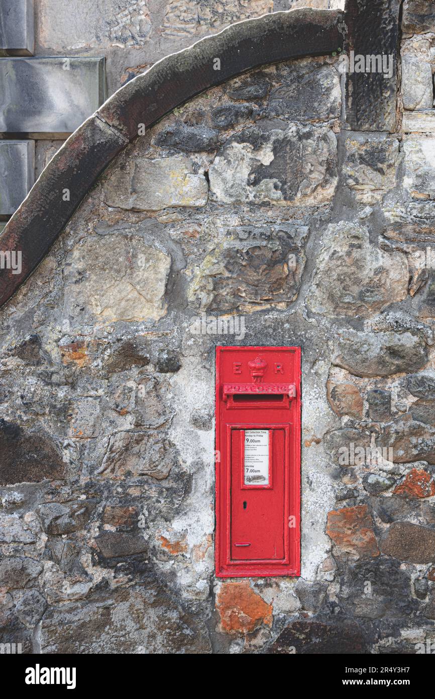 A classic, old-fashioned, vintage red letterbox or post box used by royal mail built into an old stone wall in the historic Scottish village of Aberdo Stock Photo