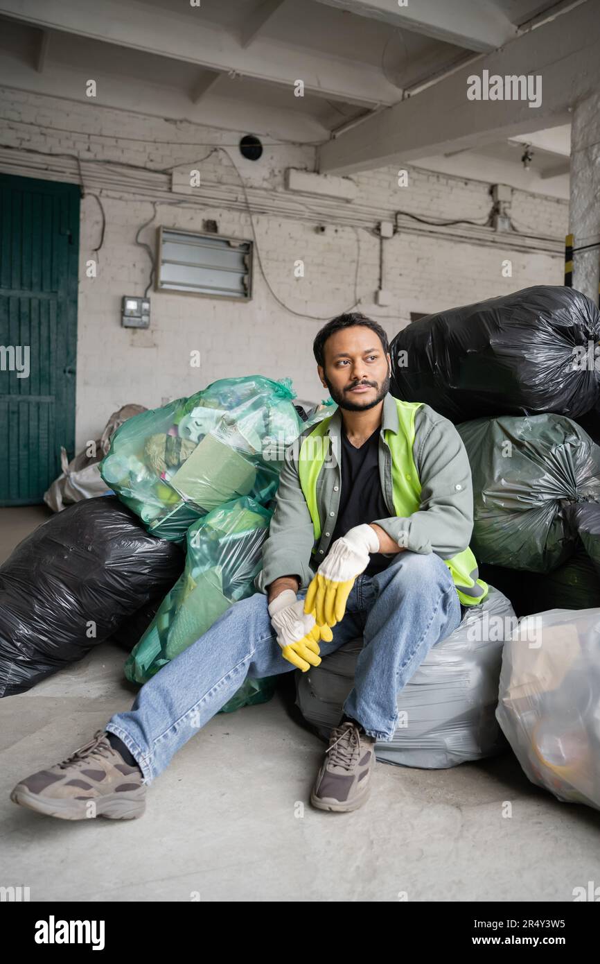 Male indian worker in high visibility vest and protective gloves sitting on plastic bags with trash while working in garbage sorting center recycling Stock Photo Alamy
