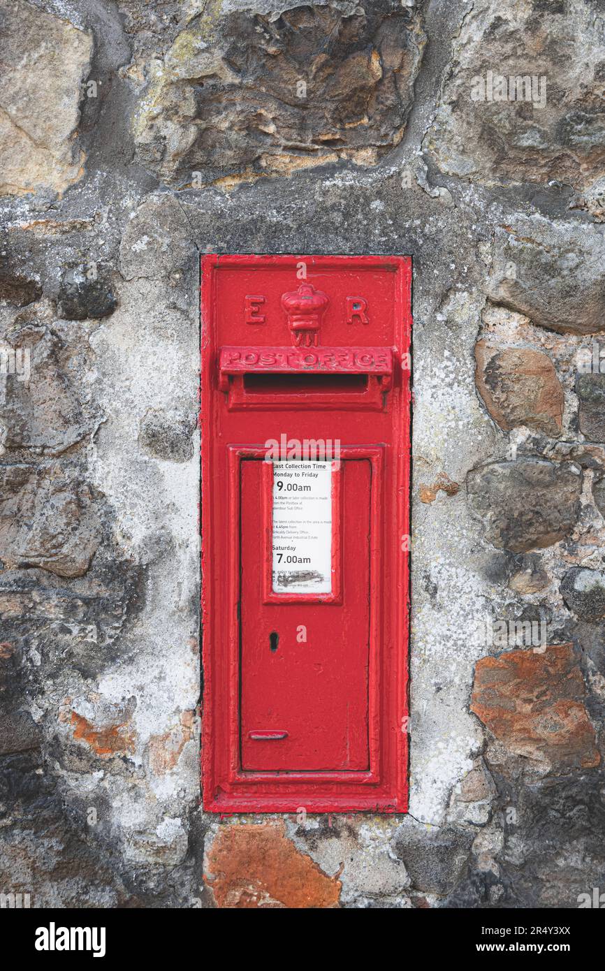 A classic, old-fashioned, vintage red letterbox or post box used by royal mail built into an old stone wall in the historic Scottish village of Aberdo Stock Photo