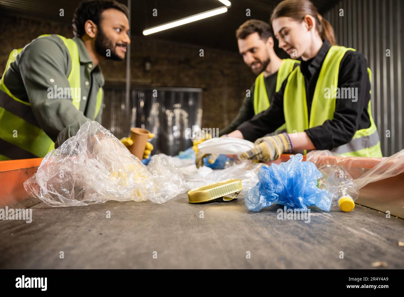 Plastic trash on conveyor and blurred multiethnic workers in safety