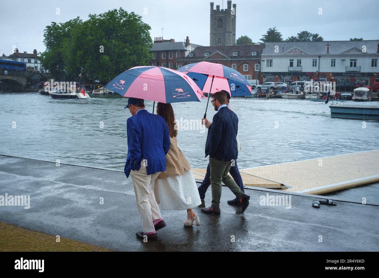 A group walk along the towpath in the rain under colourful pink and blue  Leander Club umbrellas at Henley Royal Regatta, Henley-on-Thames, 202 2 Stock Photo