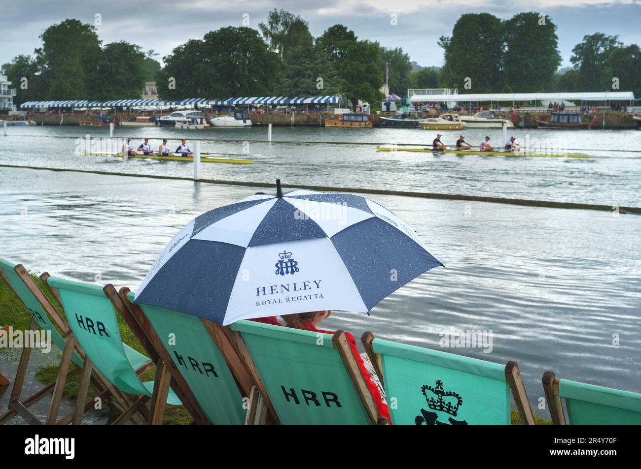 A couple shelter from the rain under a colourful blue and white umbrella  at Henley Royal Regatta, Henley-on-Thames, 2022 Stock Photo