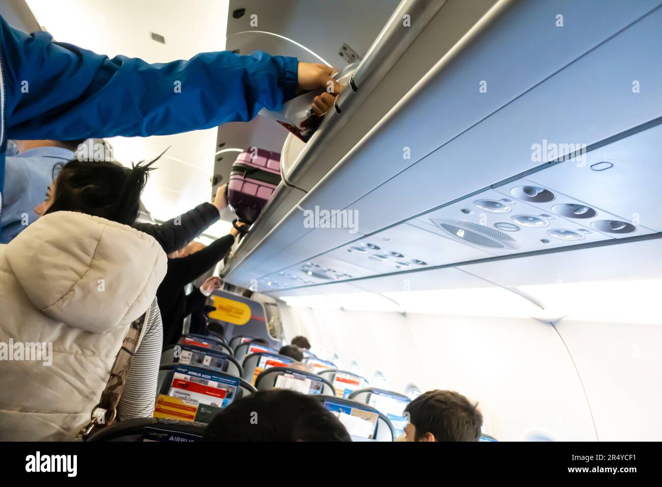 Passengers taking carry-on luggage from the overhead buggage space inside Airbus A320 airplane Stock Photo