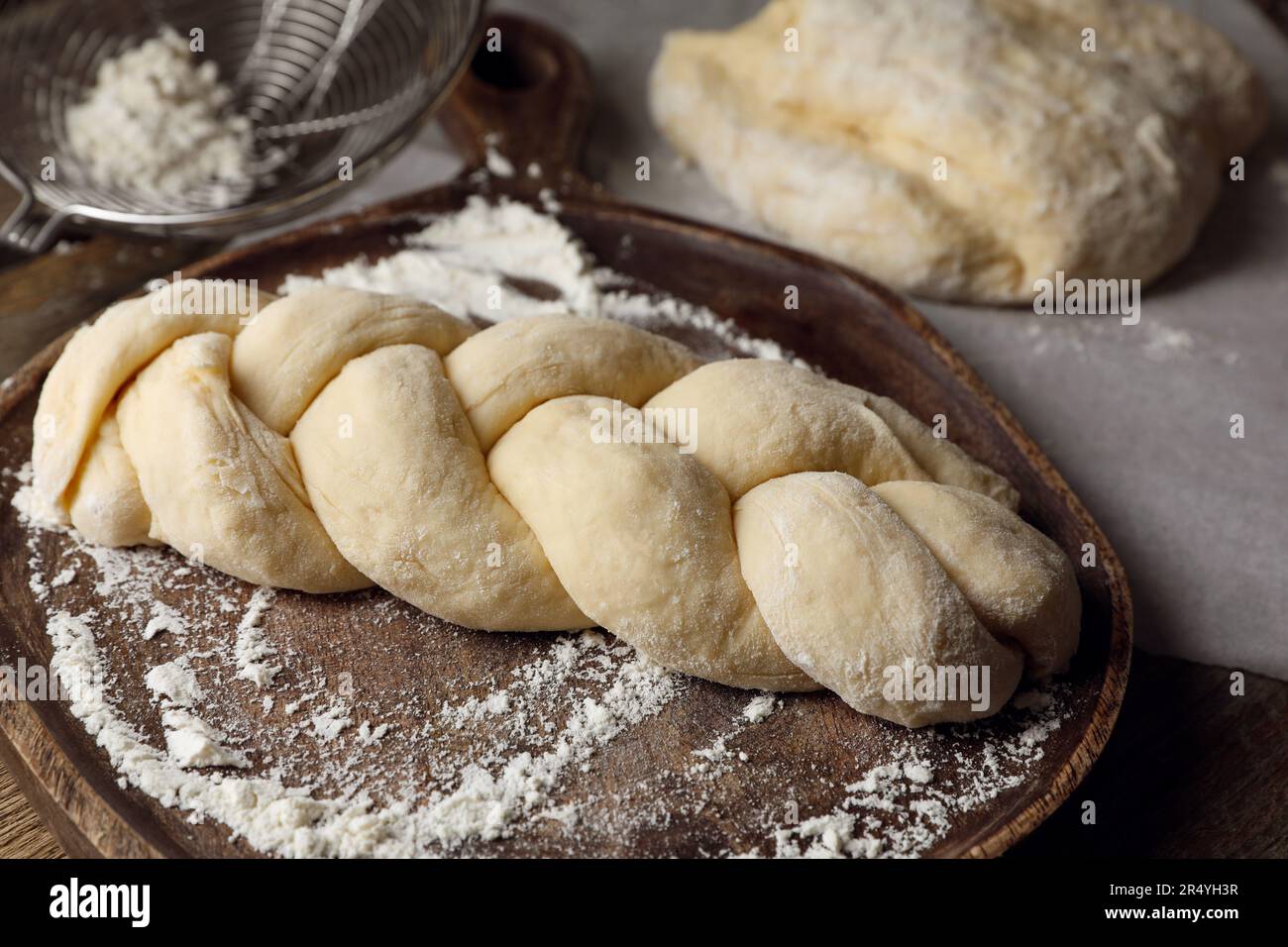 Raw braided bread and flour on wooden table, closeup. Traditional Shabbat challah Stock Photo