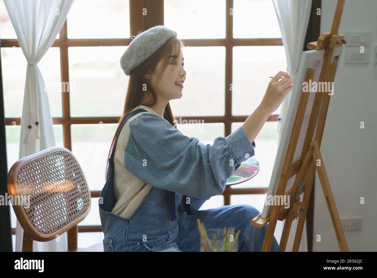 Young female painter holds color palette and use brush to painting ...