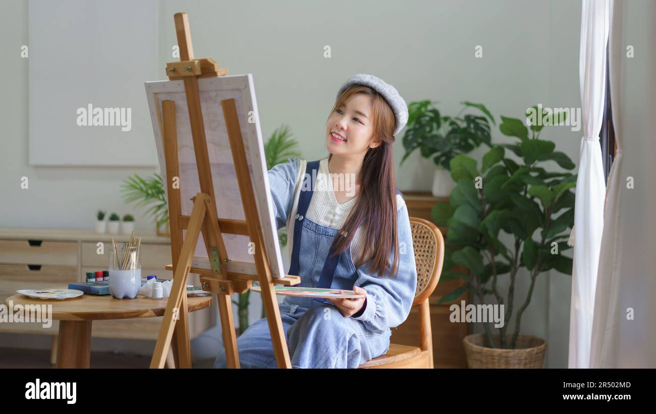 Young female artist holds color palette and use brush to painting ...