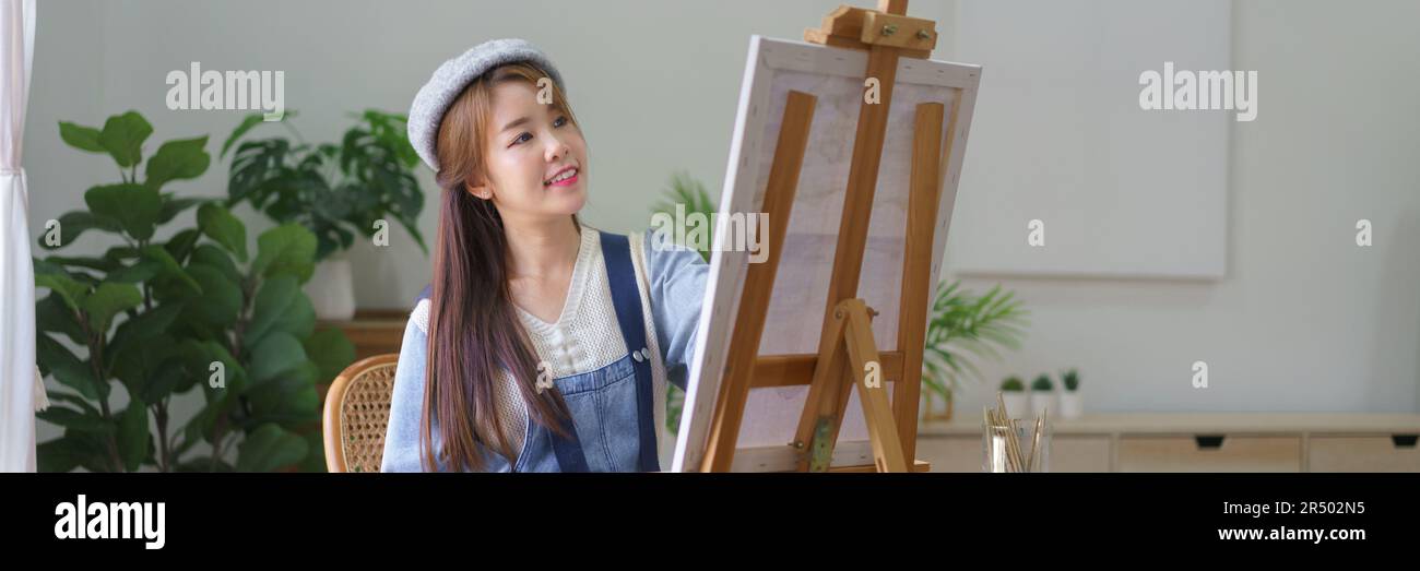 Young female artist holds color palette and use brush to painting ...