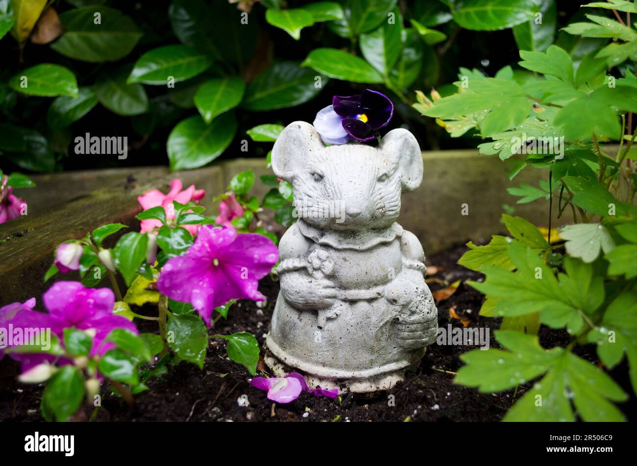 Sweet mouse garden statue in a flower bed with impatiens flowers Stock
