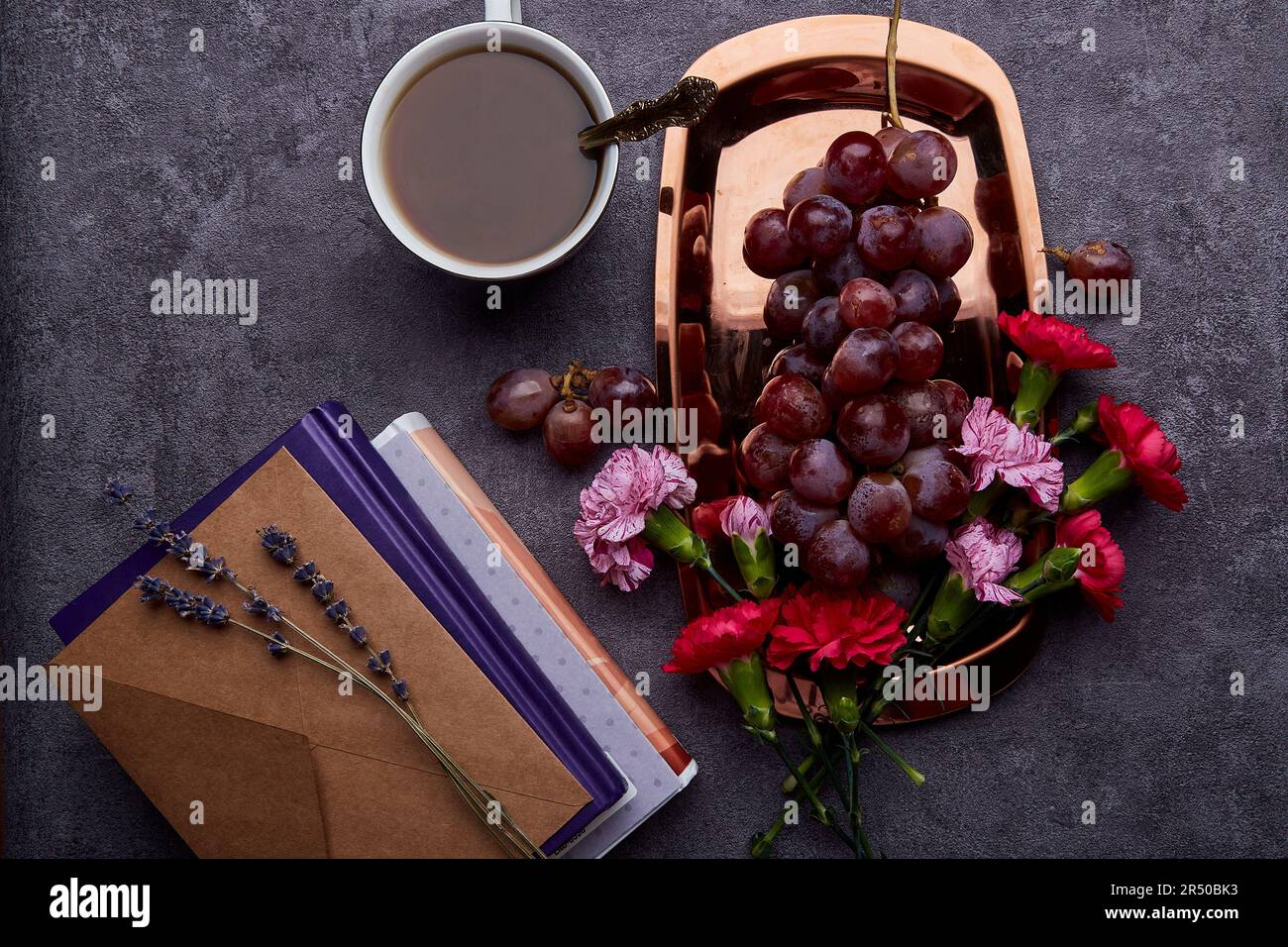 Summer flat lay breakfast with grapes, cup of coffee, books and flowers on the golden tray. Stock Photo