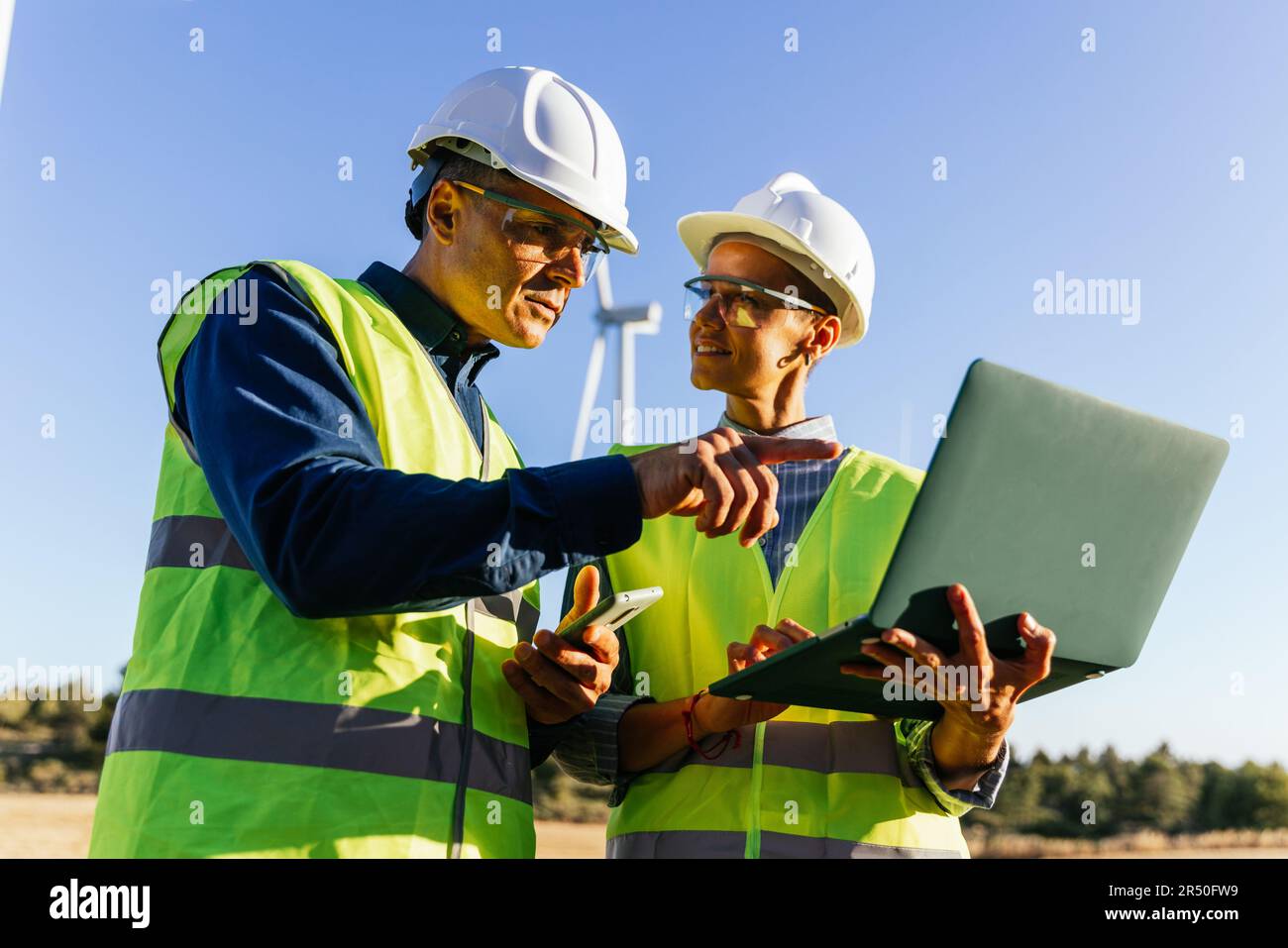 Engineers using a laptop while working together in the wind farm. Stock Photo