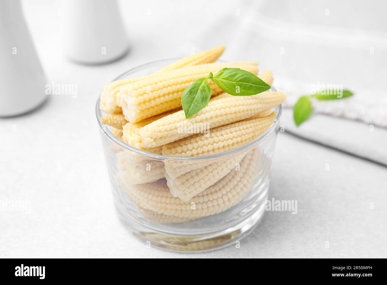 Canned baby corns with basil on white table, closeup Stock Photo