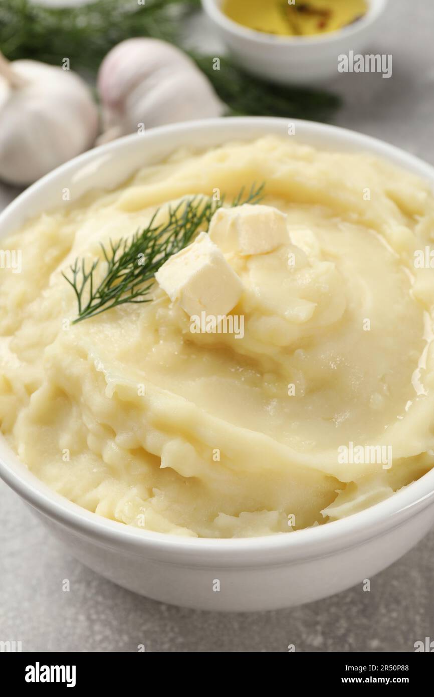 Bowl of delicious mashed potato with dill and butter on light grey table, closeup Stock Photo