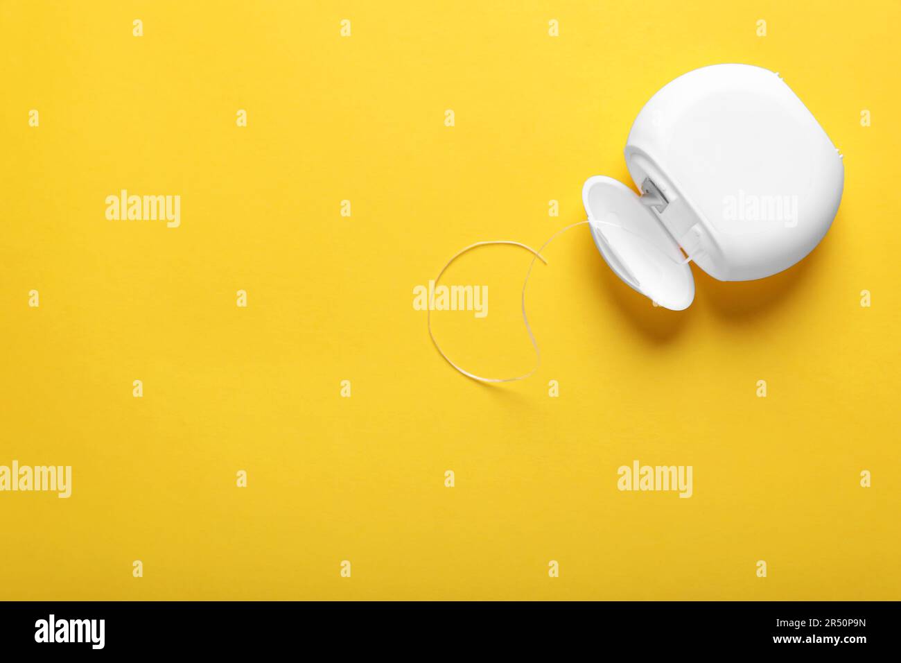 Container with dental floss on yellow background, top view. Space for