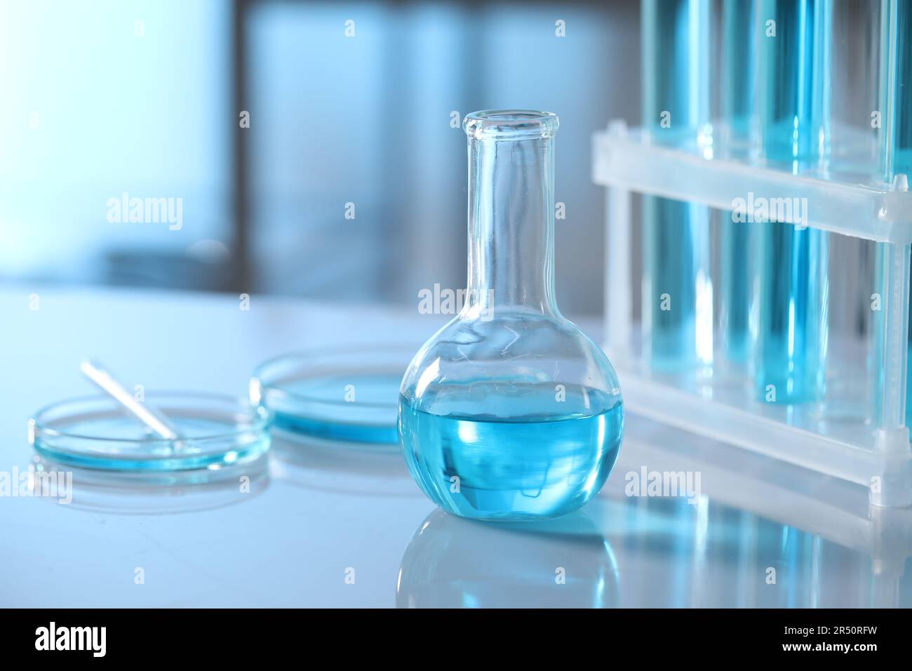 Different glassware and test tubes with light blue liquid on table in ...