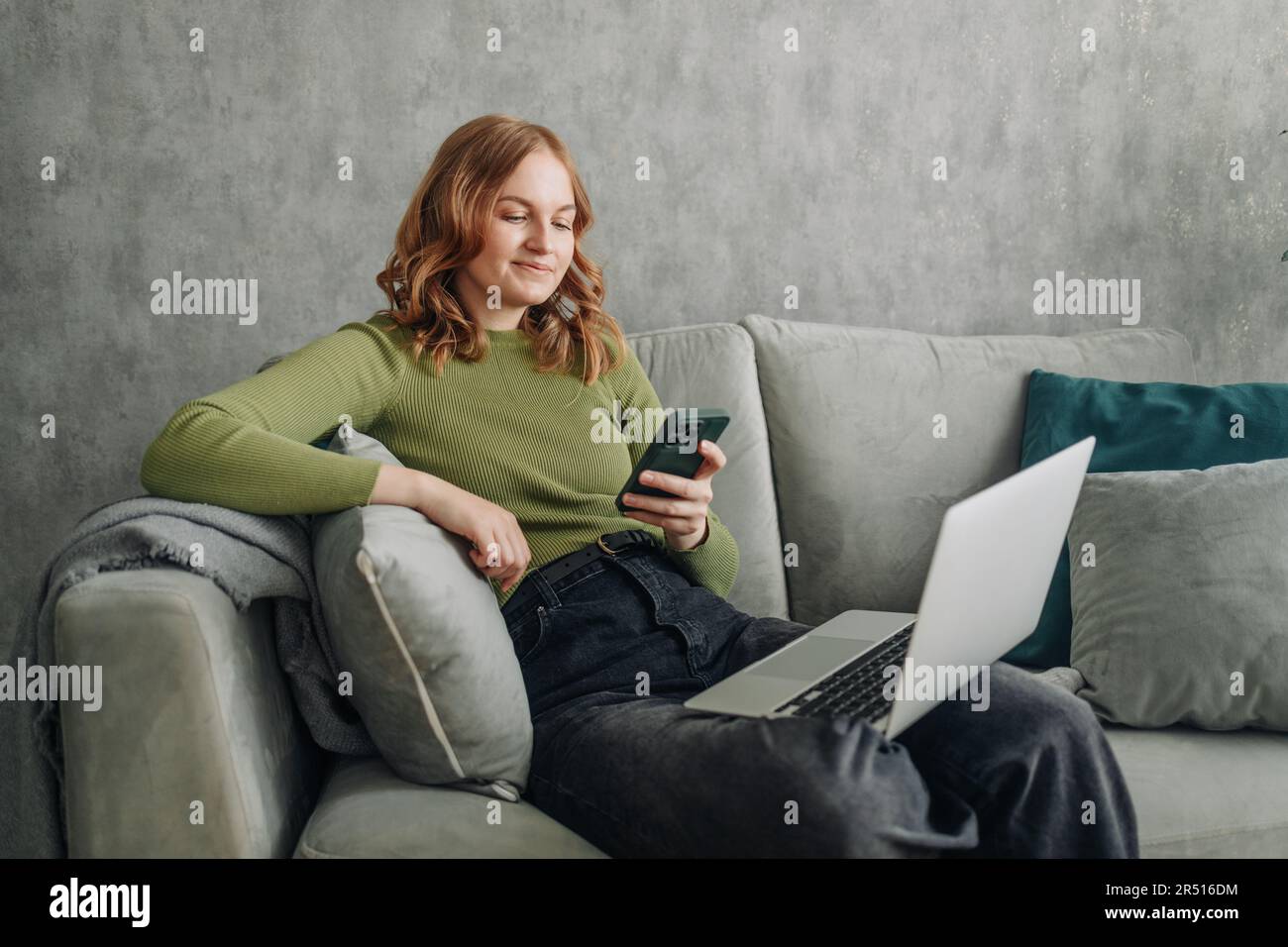 Happy relaxed young woman sitting on couch using cell phone, smiling ...