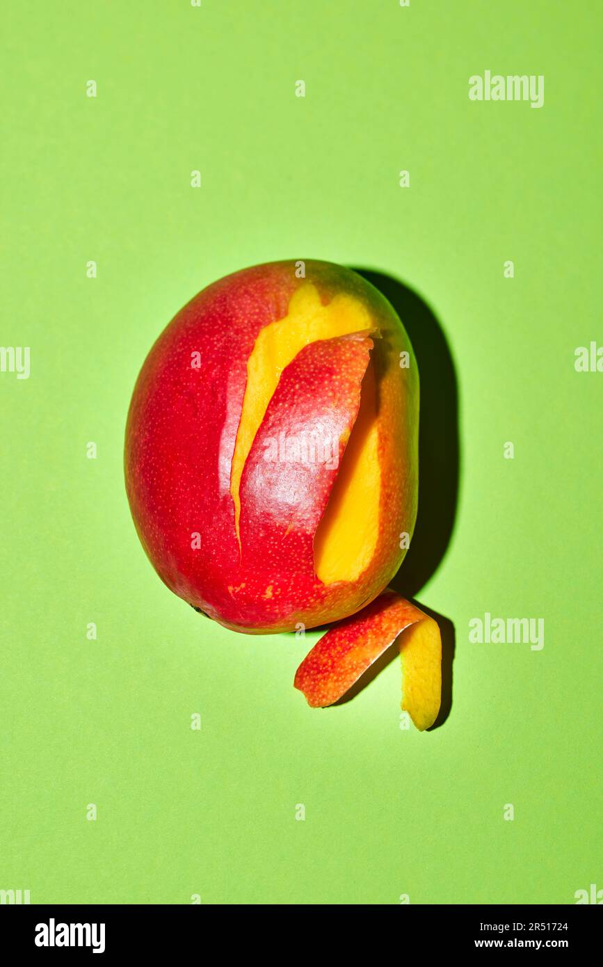 Partially peeled mango on a green background Stock Photo - Alamy