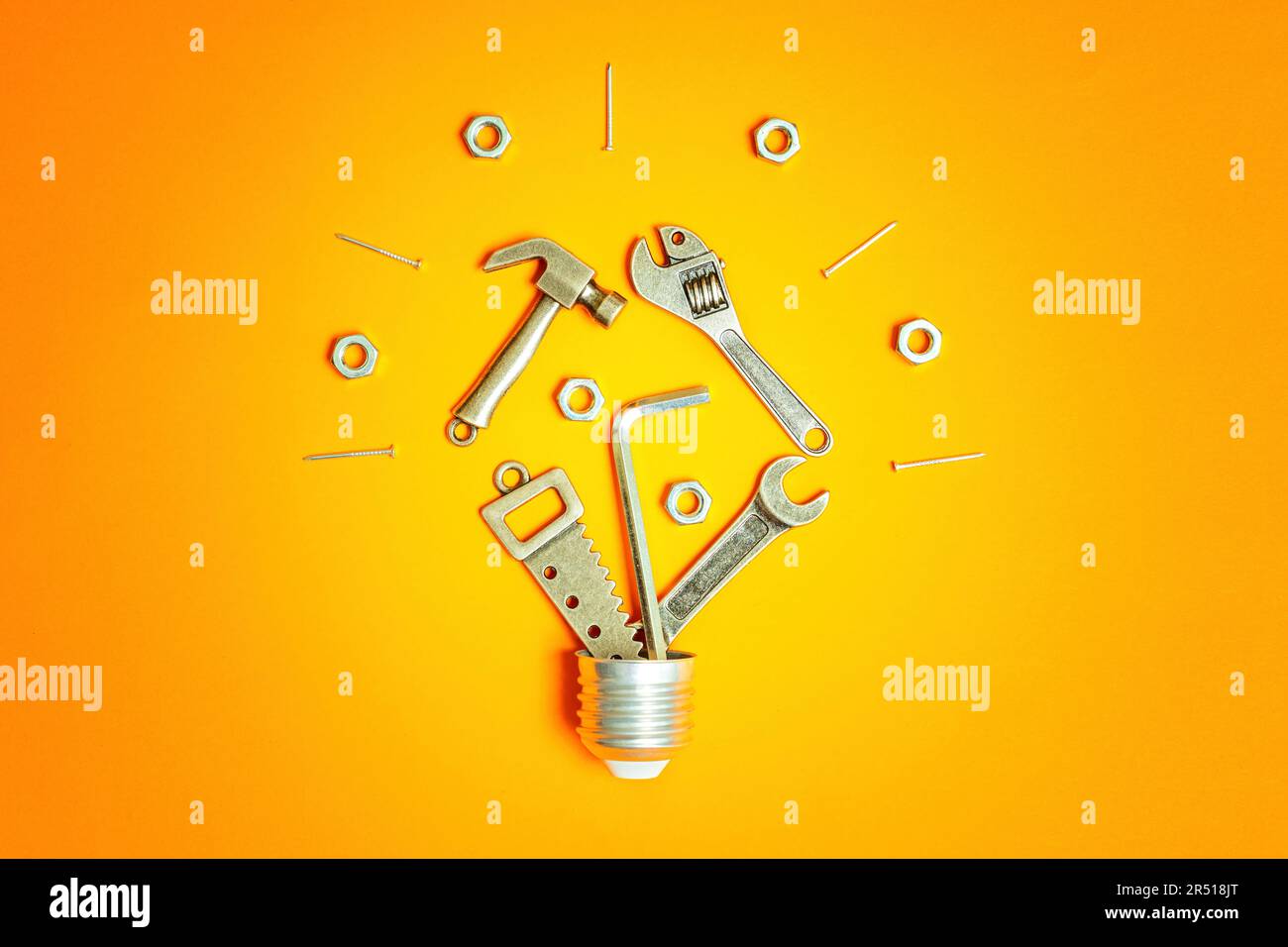 Lightbulb symbol made from tiny steel replicas of various hand tools and fasteners, all arranged on a vibrant orange background. Construction, enginee Stock Photo