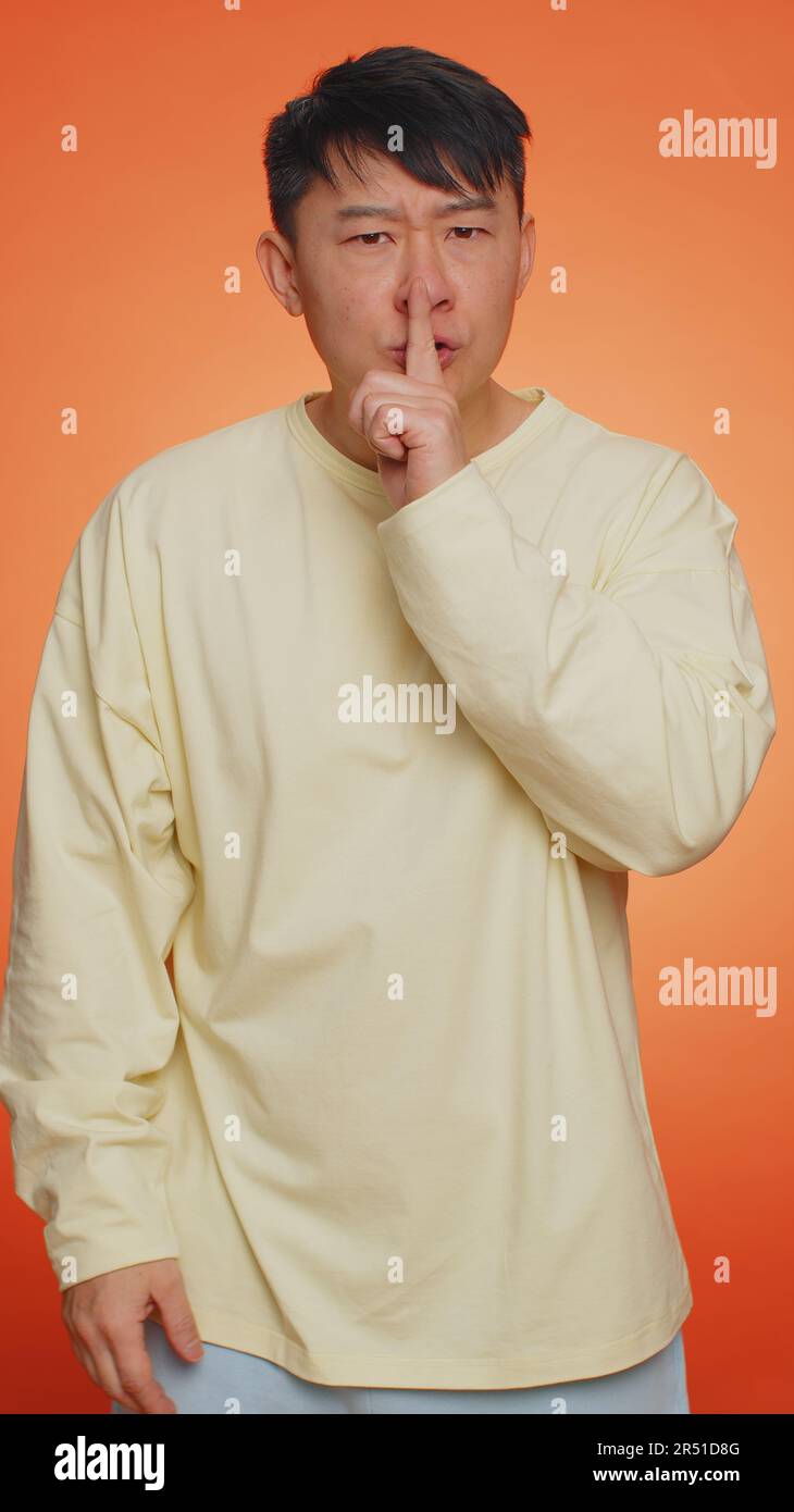 Keep my secret. Do not tell anyone. Shh be quiet please. Asian man presses index finger to lips