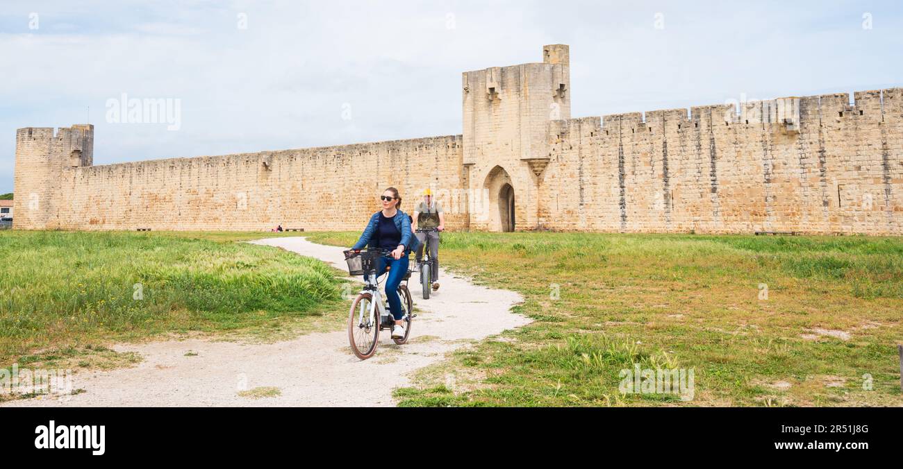 Aigues-Mortes, France - April 28, 2023: People cycling outside of medieval city town  of  Aigues Mortes with its well preserved wall and ramparts Stock Photo