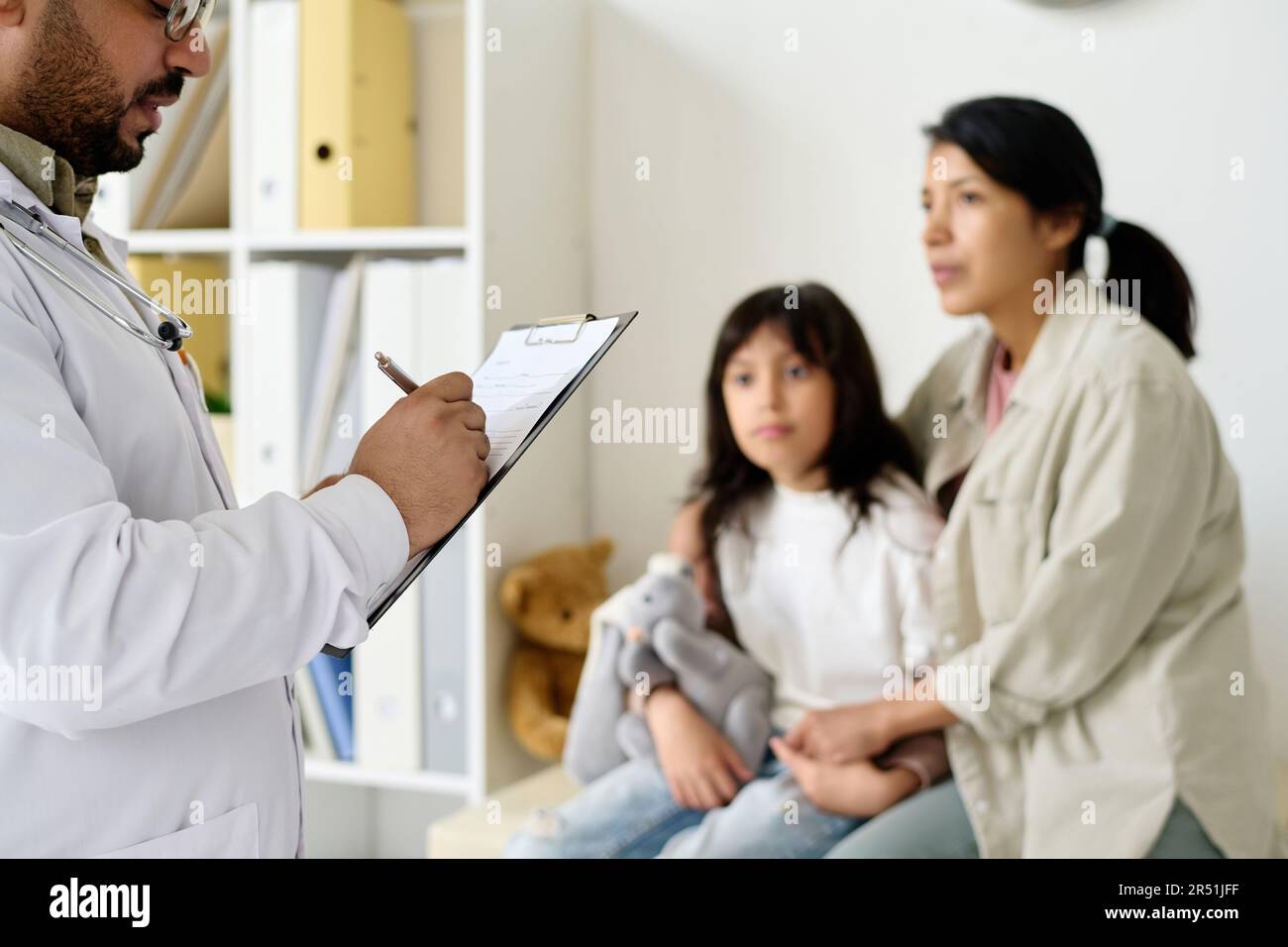 Doctor prescribing medicine to child making notes in medical card with ...
