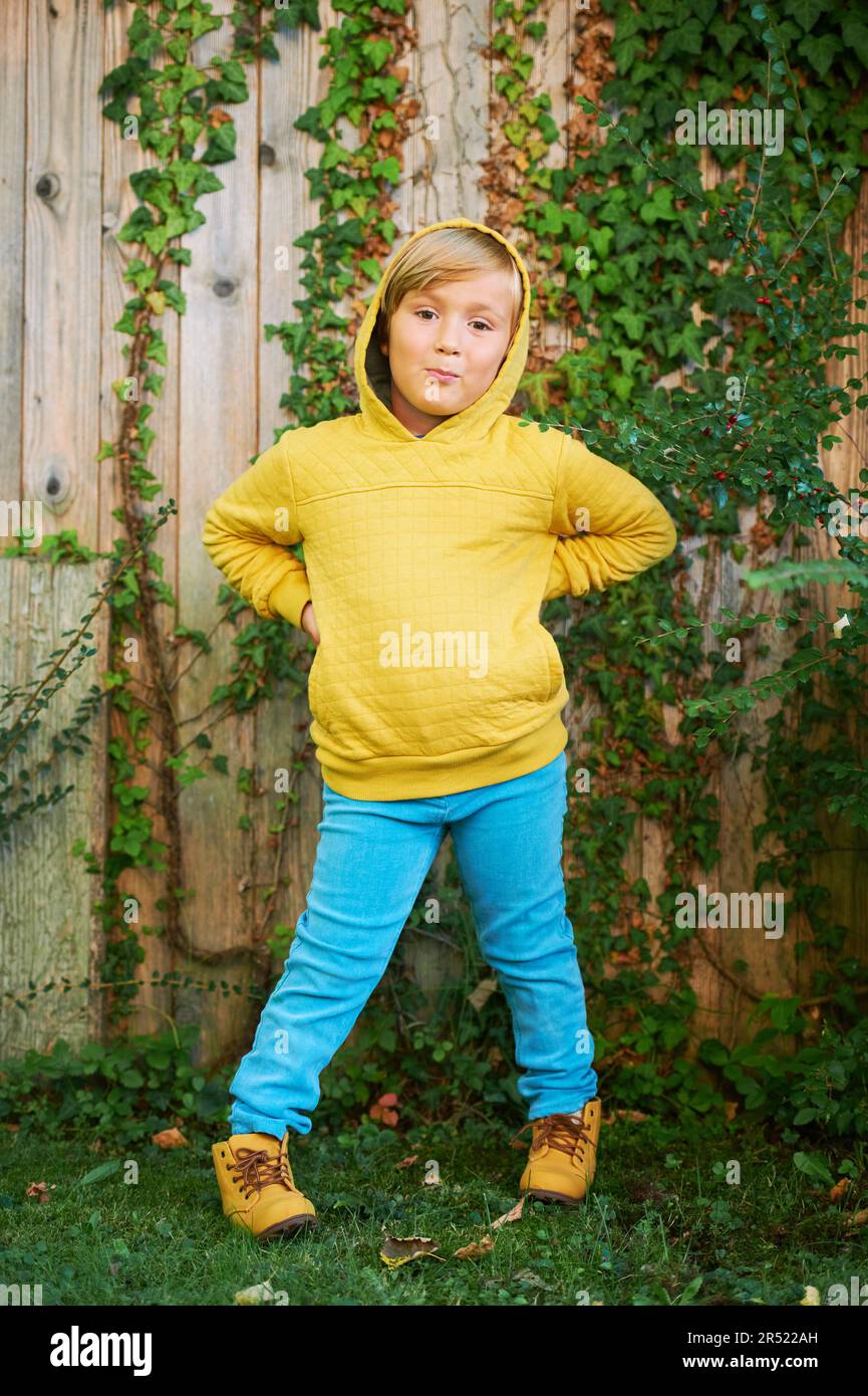 Outdoor portrait of adorable 5 year old boy wearing yellow hoodie and turquoise jeans Stock Photo