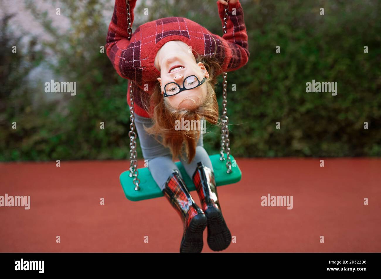 Outdoor porrait of funny little girl playing on swing, looking upside
