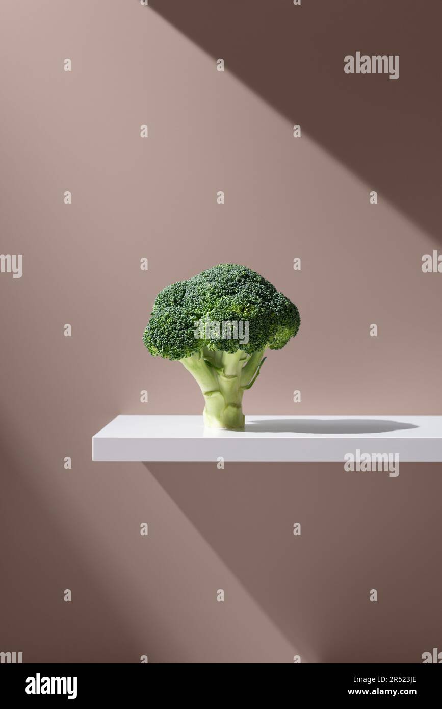 Fresh bunch of broccoli with green leaves placed over white table on brown background in studio under bright ray of light Stock Photo